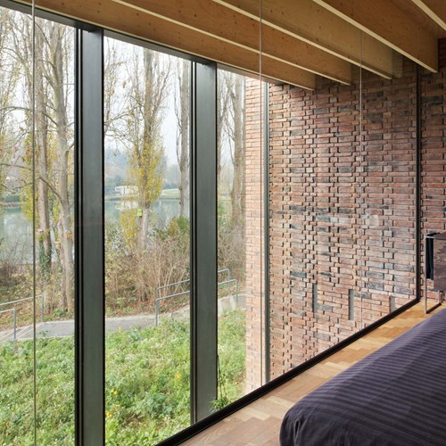 ruime slaapkamer met natuurlijke lichtinval dankzij grote zwarte aluminium ramen met grote glaspartijen