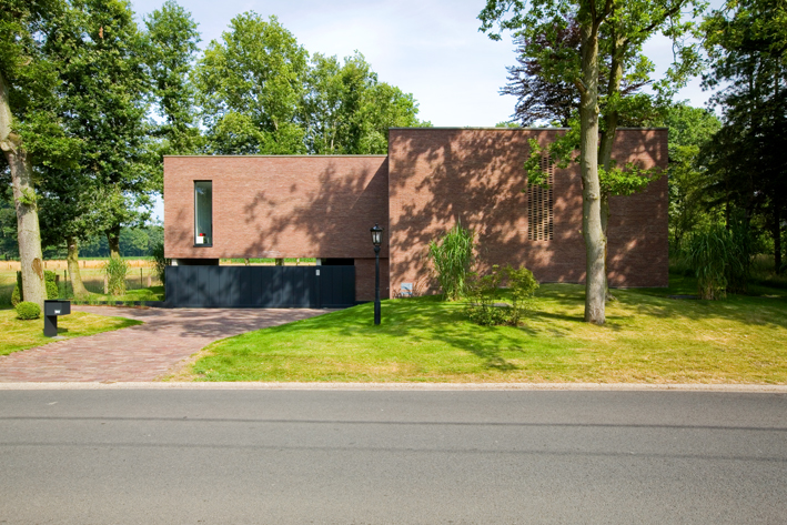 Een vierkant huis van bakstenen op een grasveld met wat bomen.
