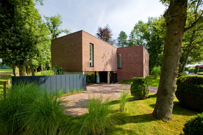 Een vierkant huis van bakstenen op een grasveld met wat bomen.
